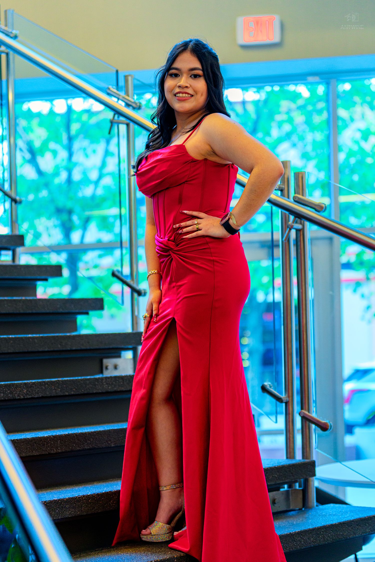 Young woman in elegant red slit gown posing on stairs at formal event.