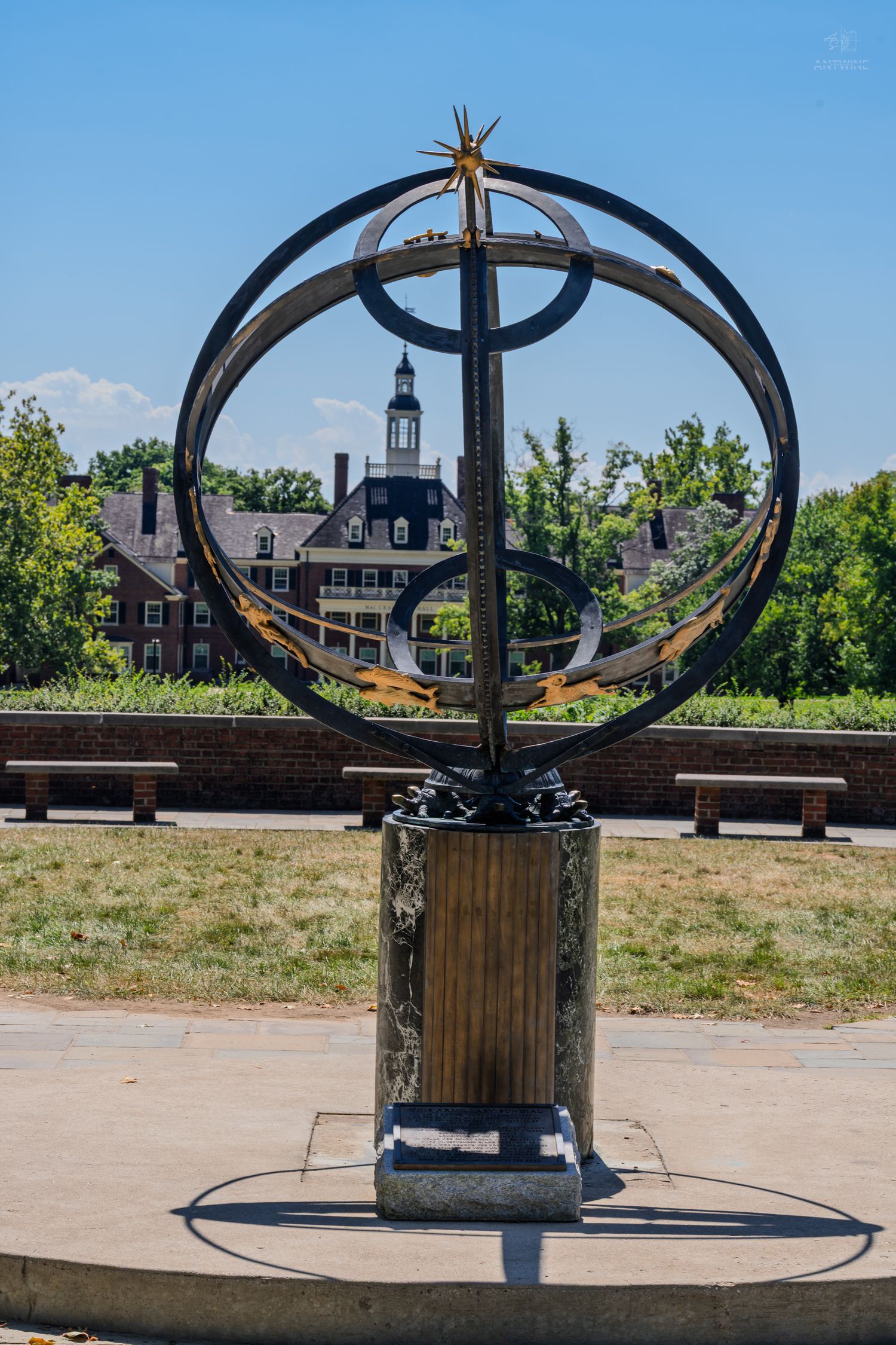 Armillary sphere sundial on stone pedestal with historic brick building and blue sky in background.