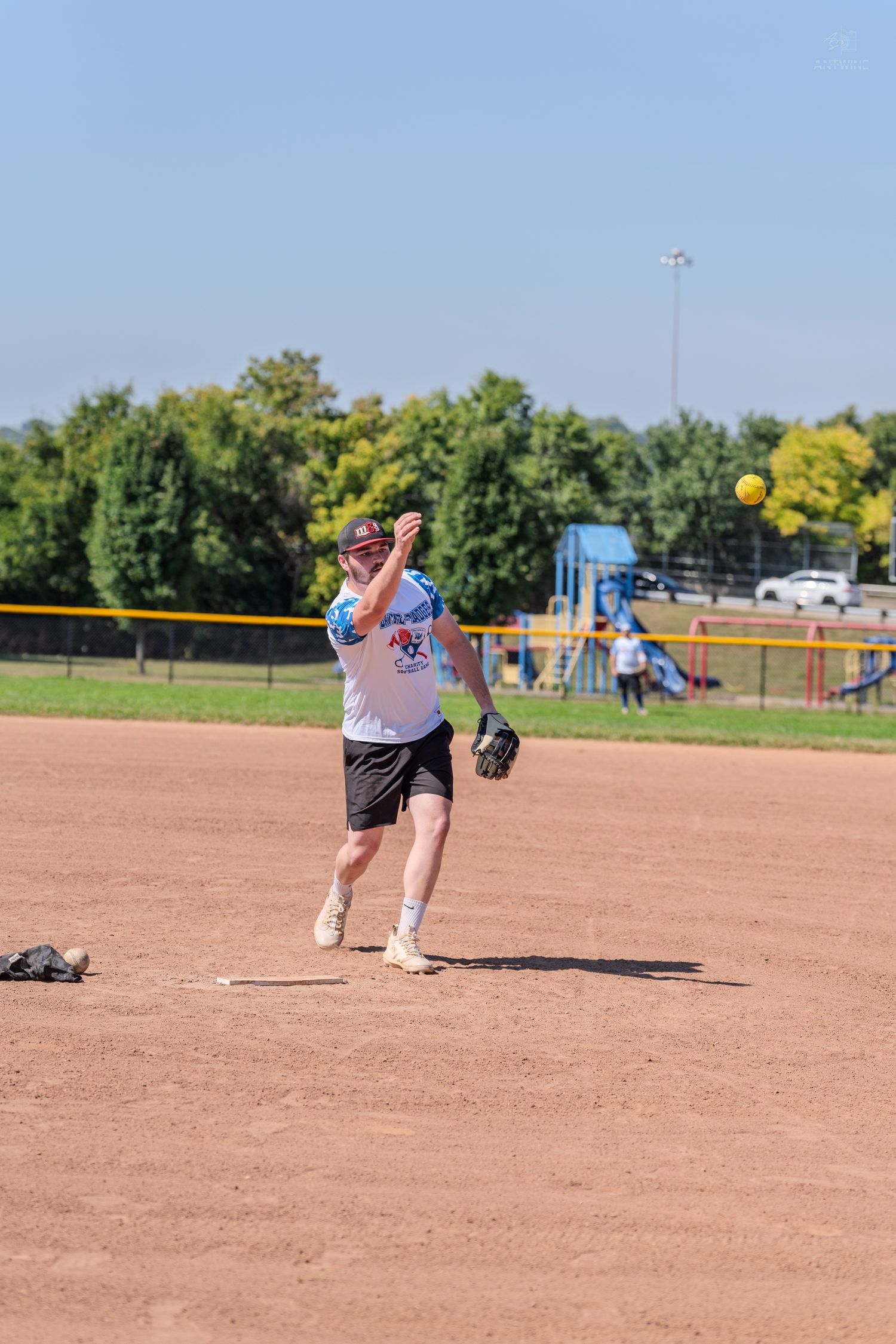 Softball player in white uniform throwing ball from infield position on sunny clear day.