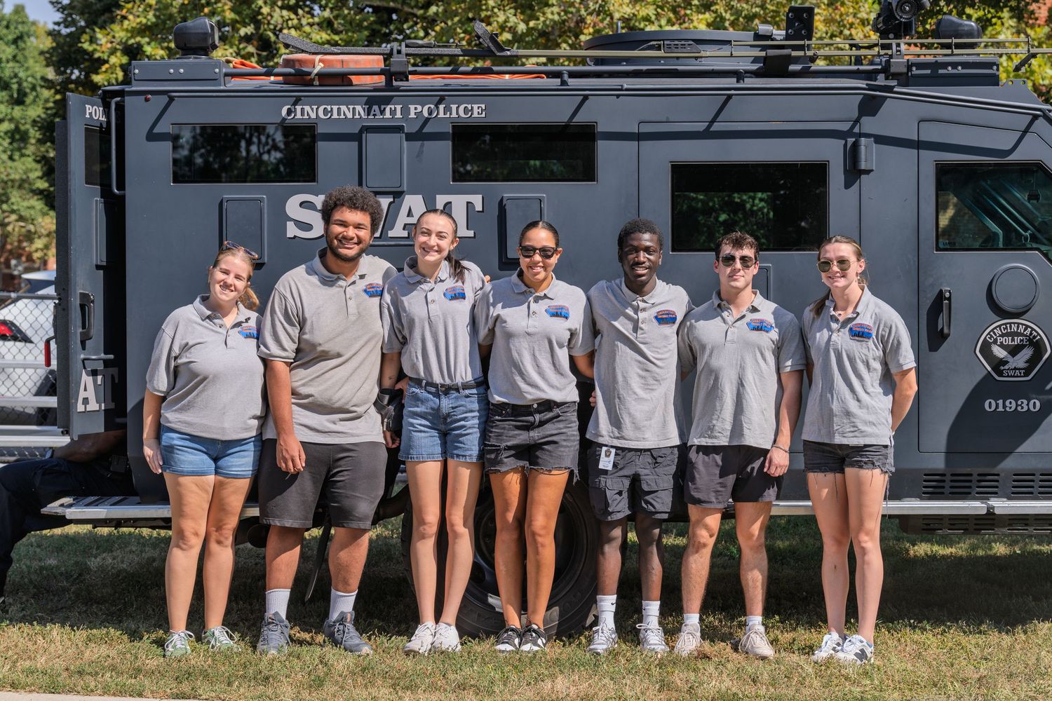 Seven people pose together in front of a Lincoln police SWAT vehicle outdoors on a sunny day.