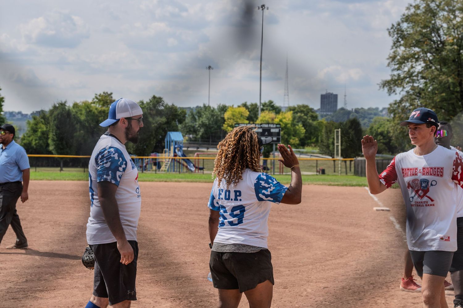 Softball players in FOP jerseys gather on field while woman records video on sunny day.