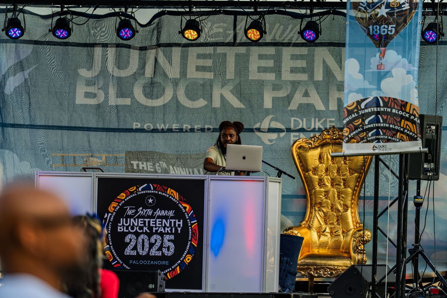 DJ performing at Juneteenth Block Party 2025 outdoor stage with colorful lights and decorative gold crown balloon.