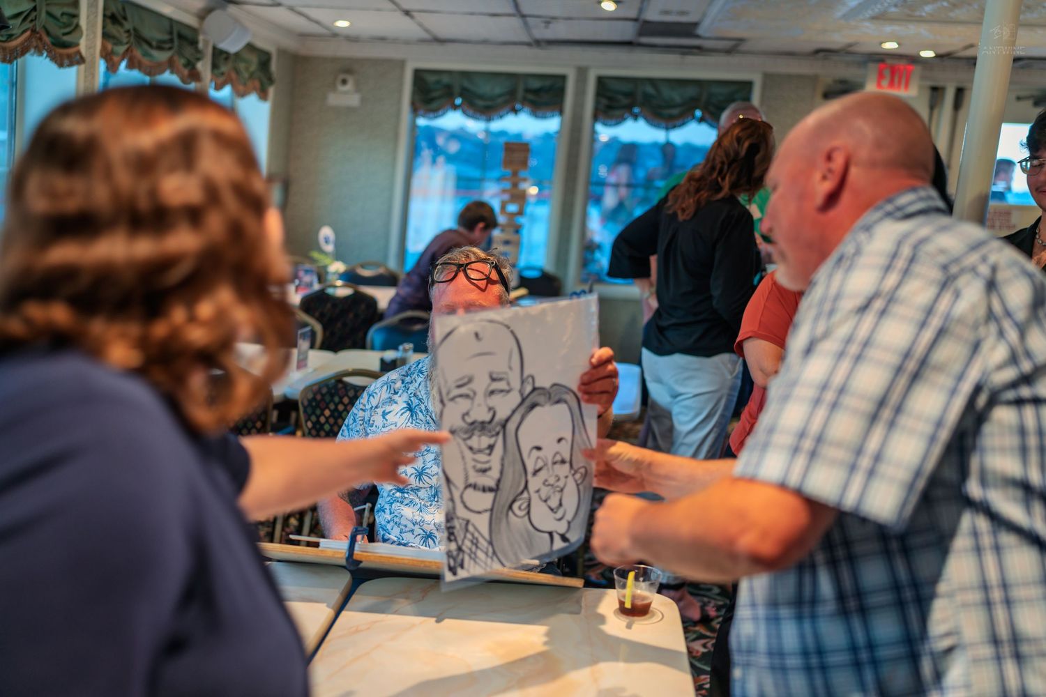 Guests admiring a black and white caricature drawing at an indoor social gathering event.