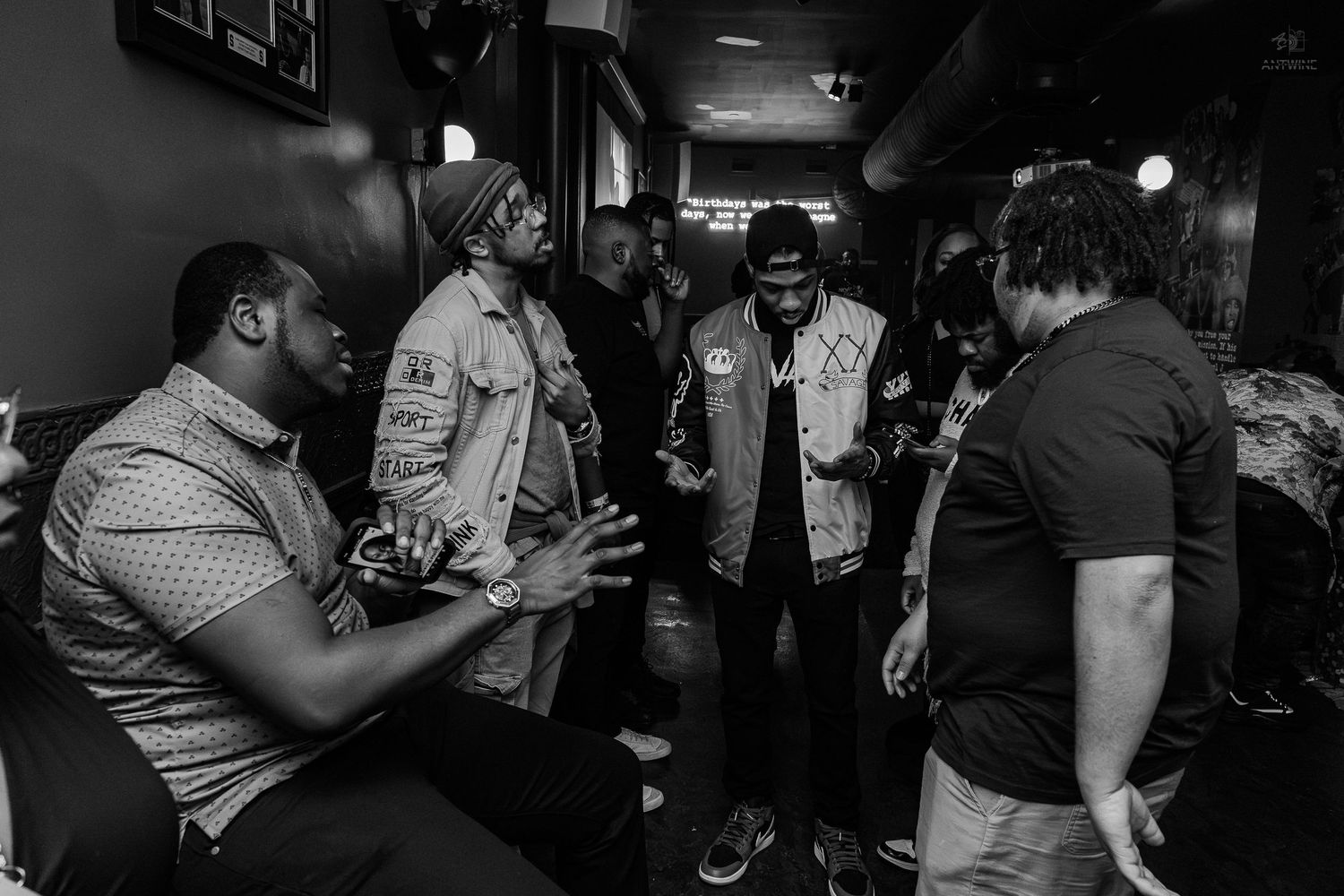 Black and white photo of a group of men having a conversation in a dimly lit backstage area.