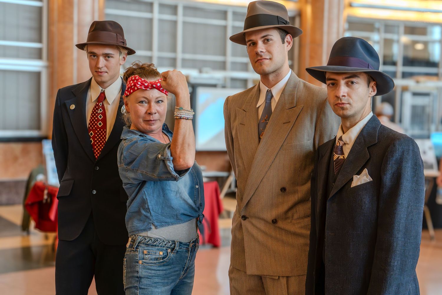 Four people in 1940s costumes pose together, including Rosie the Riveter and three men in suits and fedoras.