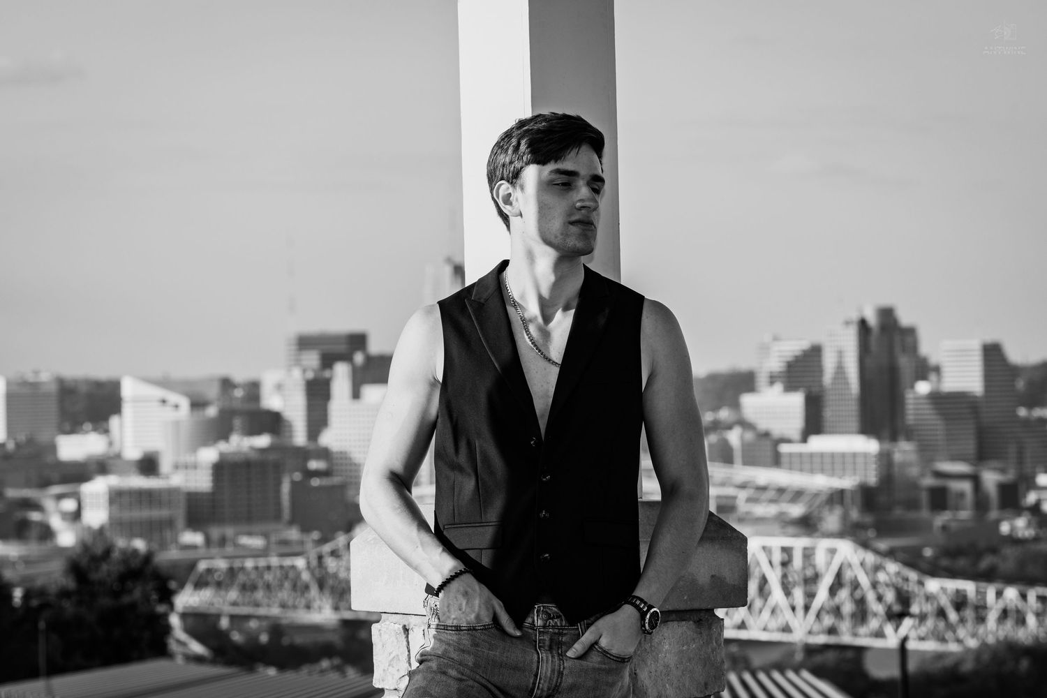 Young man in vest poses on rooftop with city skyline in black and white urban photography.