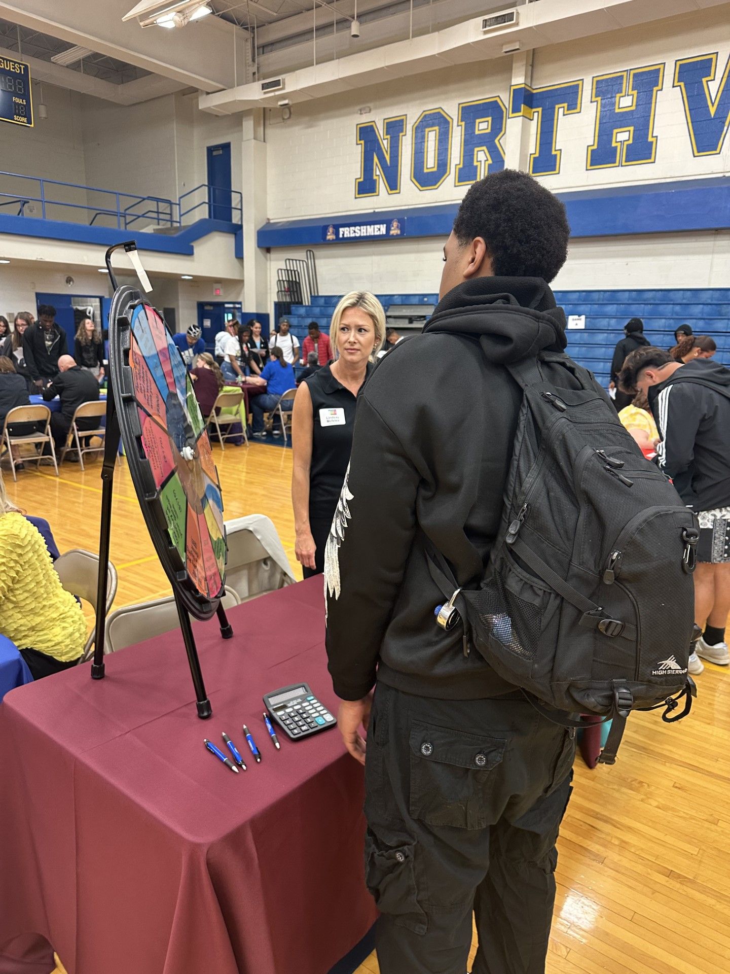 Student talks with a blonde woman at a career fair booth in a Northview school gymnasium.