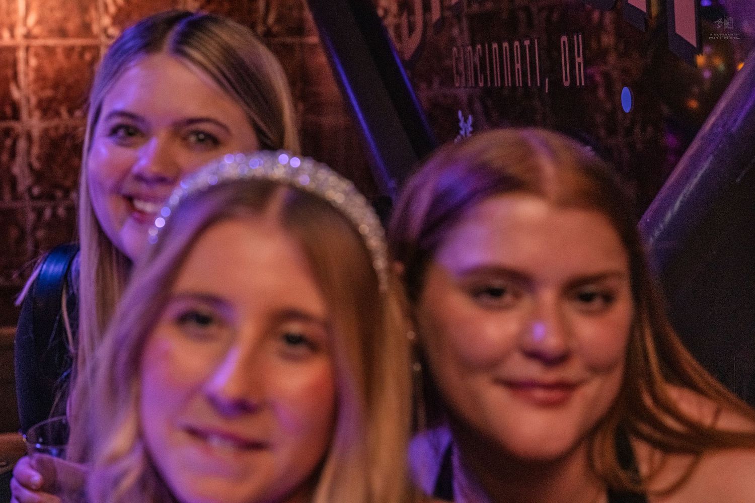 Three women posing together under warm lights at a nightclub venue.
