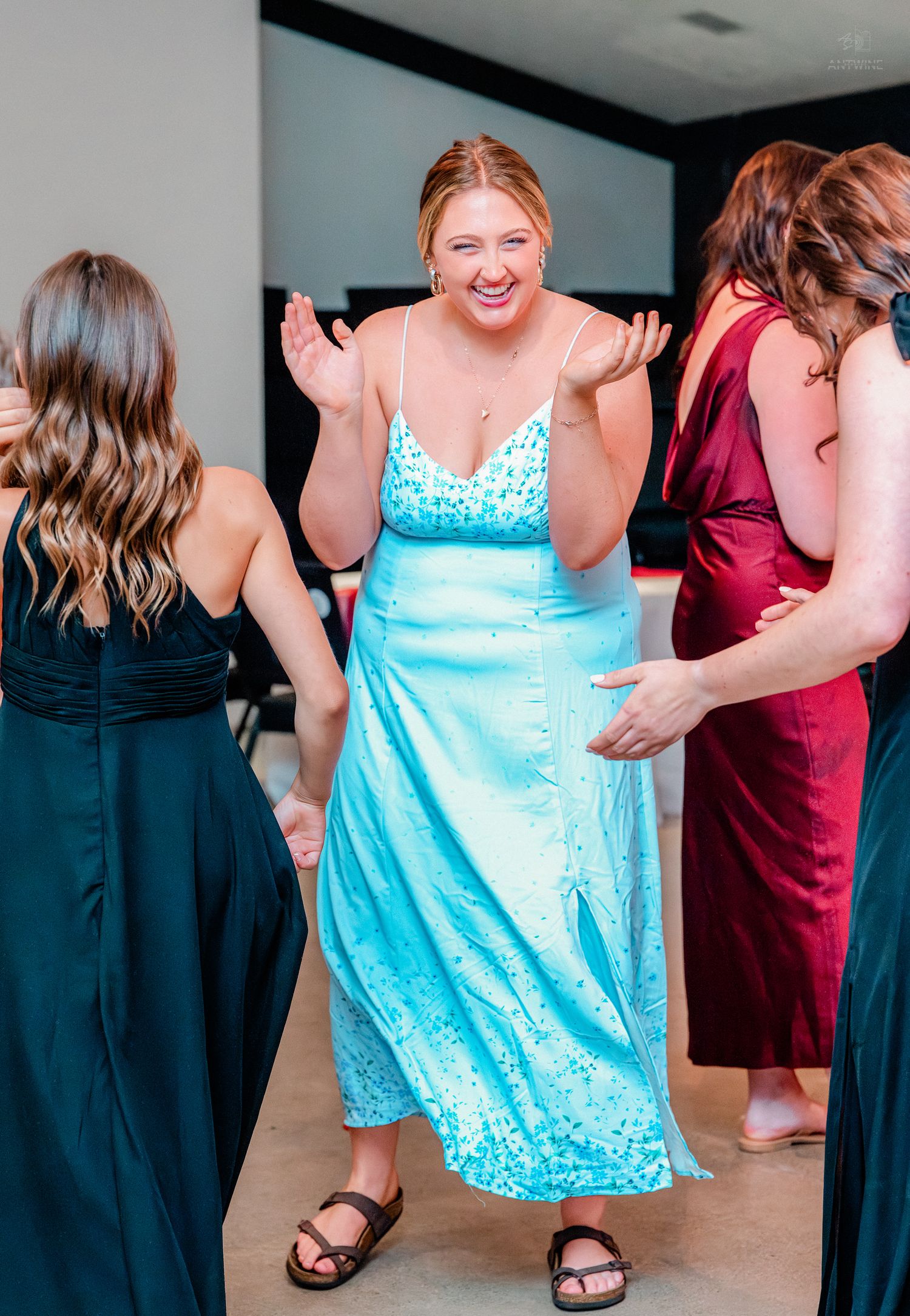 Woman in blue sequin dress laughs with bridesmaids in dark gowns at wedding celebration.