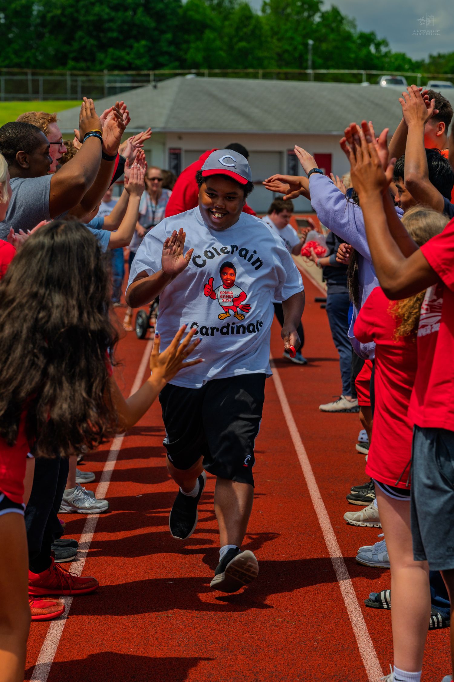Student runs through high-five tunnel at Colerain Cardinals school track event, surrounded by cheering peers.