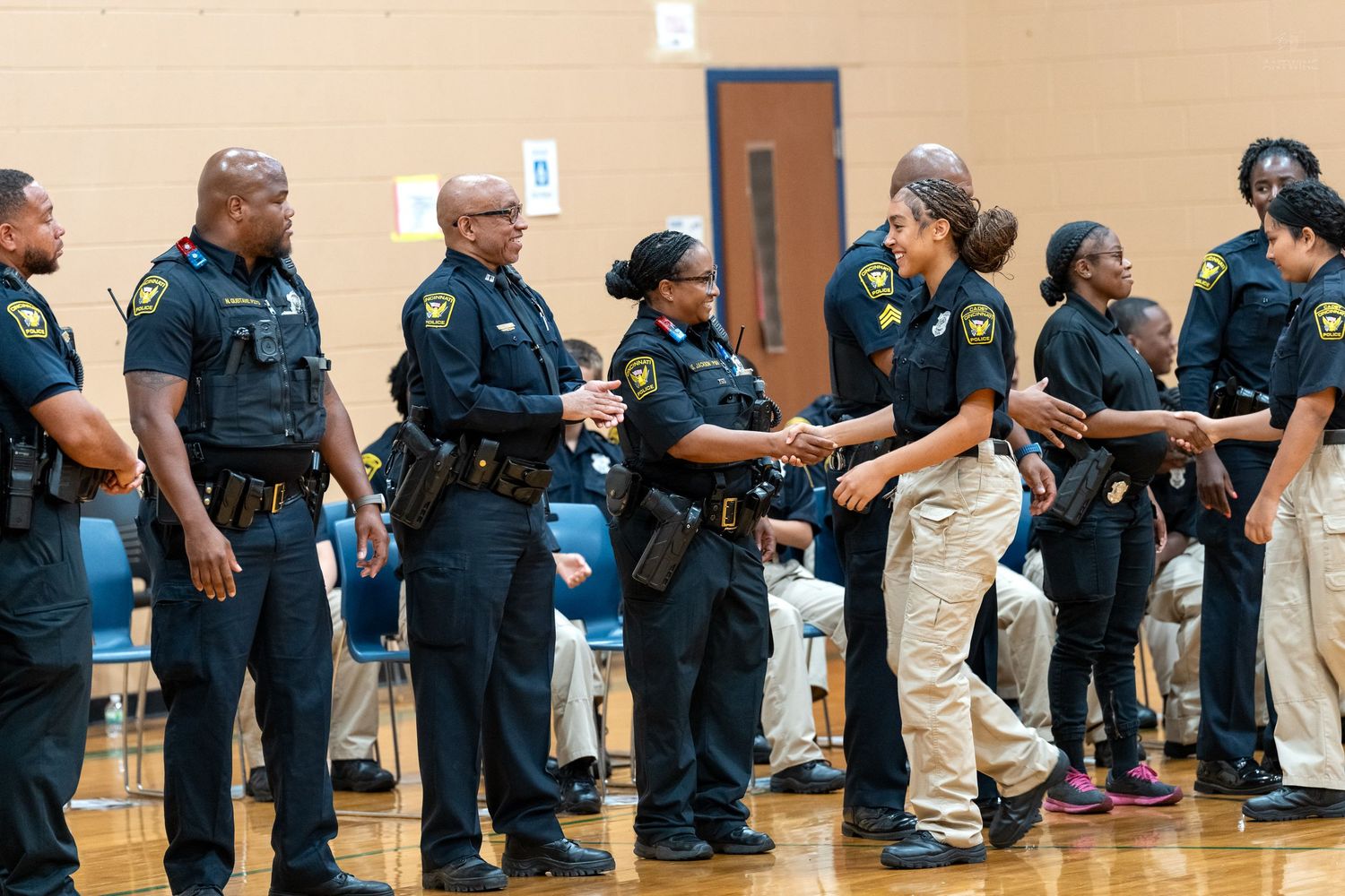Police officers in black uniforms line up indoors, shaking hands during an official law enforcement ceremony.