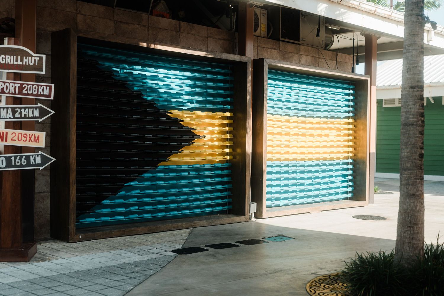 Colorful Bahamian flag painted on closed storefront shutters near a tropical shopping area.