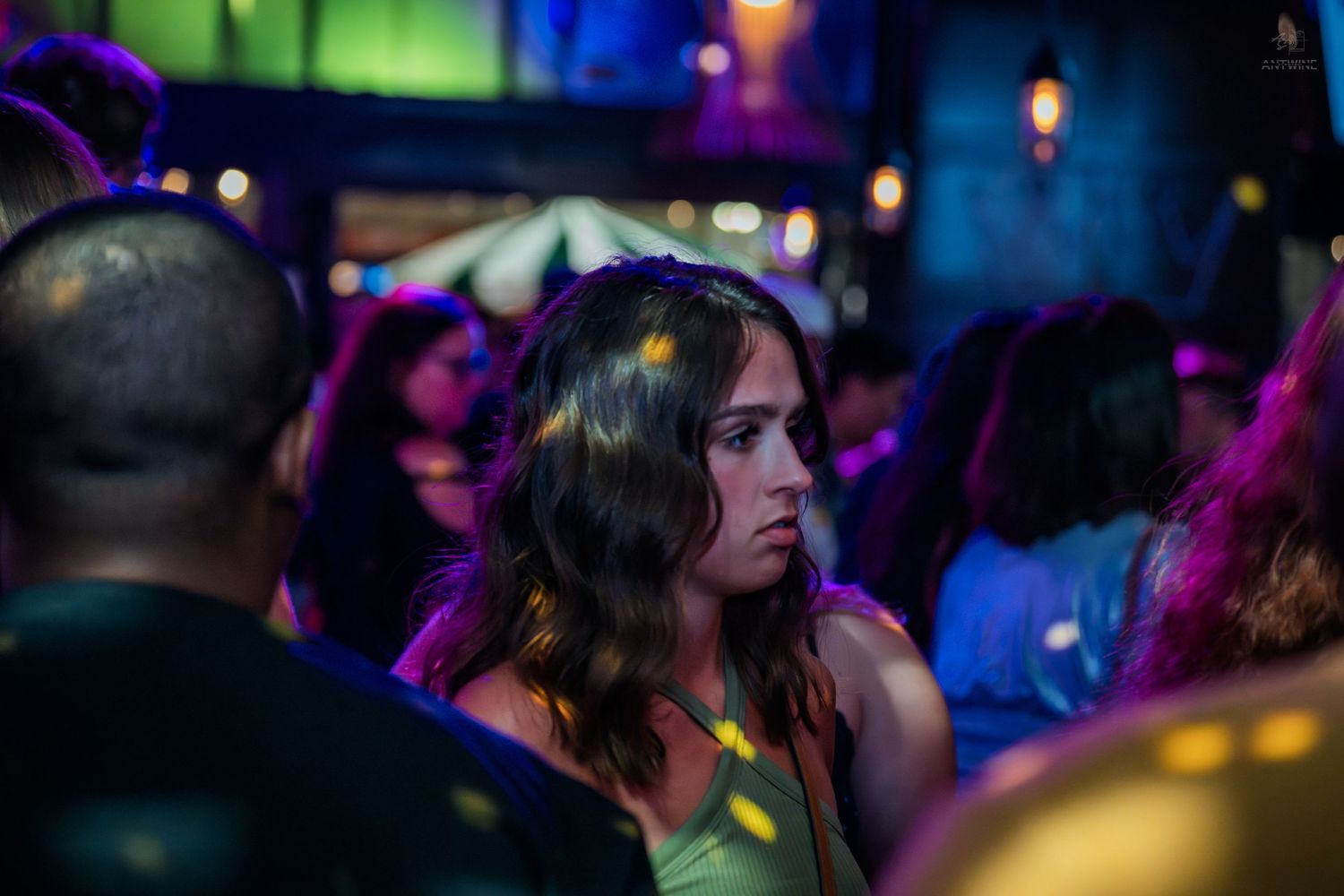 Young woman with long brown hair looking pensive in a crowded nightclub.