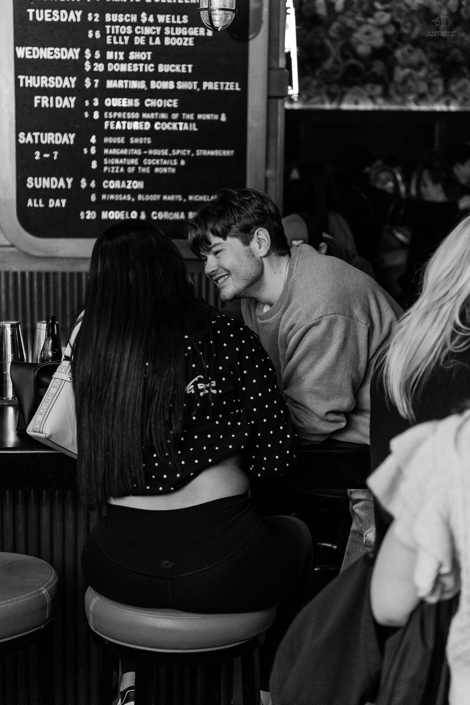 Couple sharing an intimate moment at a bar counter with a weekly specials menu board behind them.
