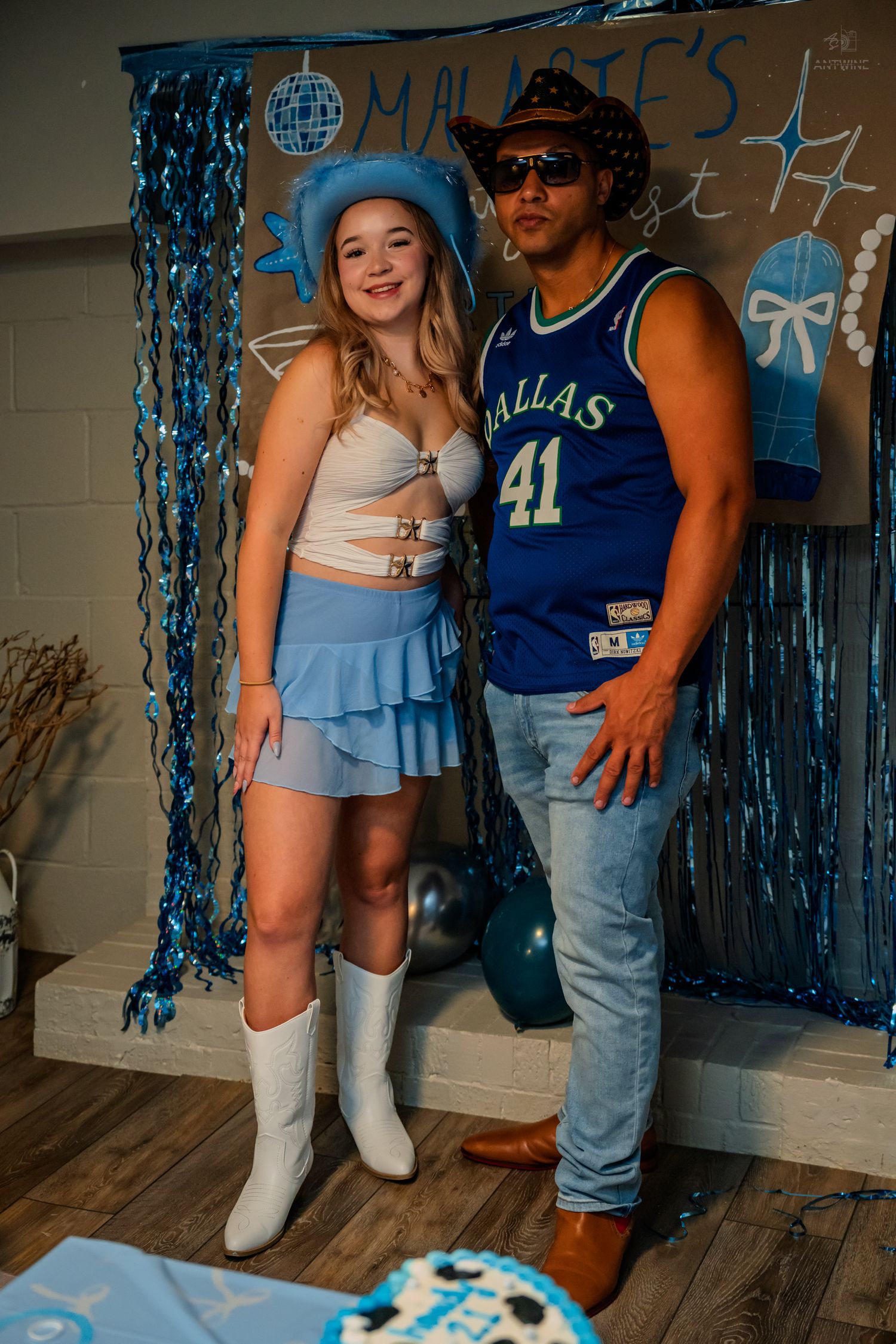 Two friends pose at Malarie's 21st birthday party, wearing blue cowboy hat and Dallas Mavericks jersey with blue decorations.