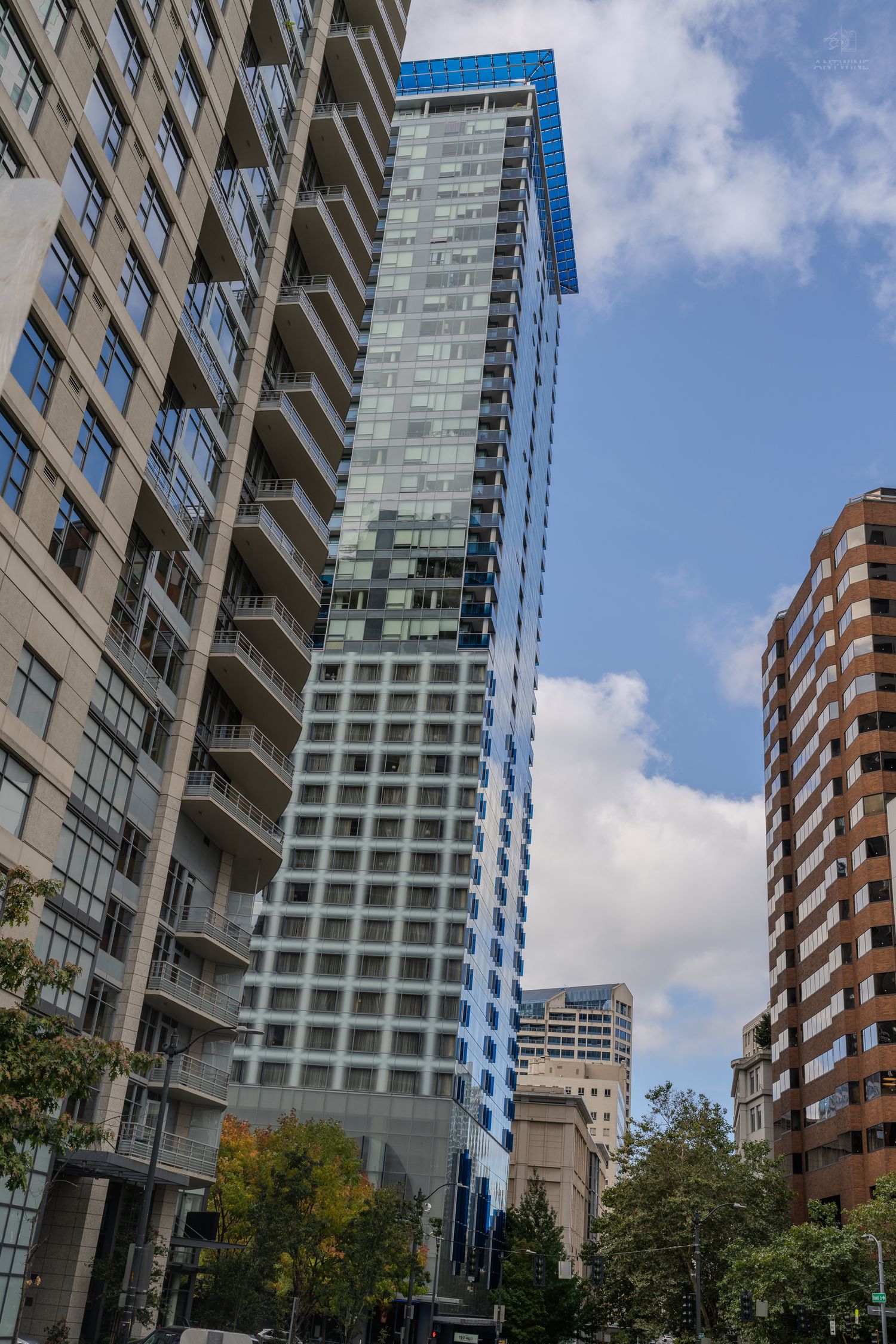 Tall modern glass skyscraper towers above surrounding buildings in downtown Seattle under partly cloudy skies.