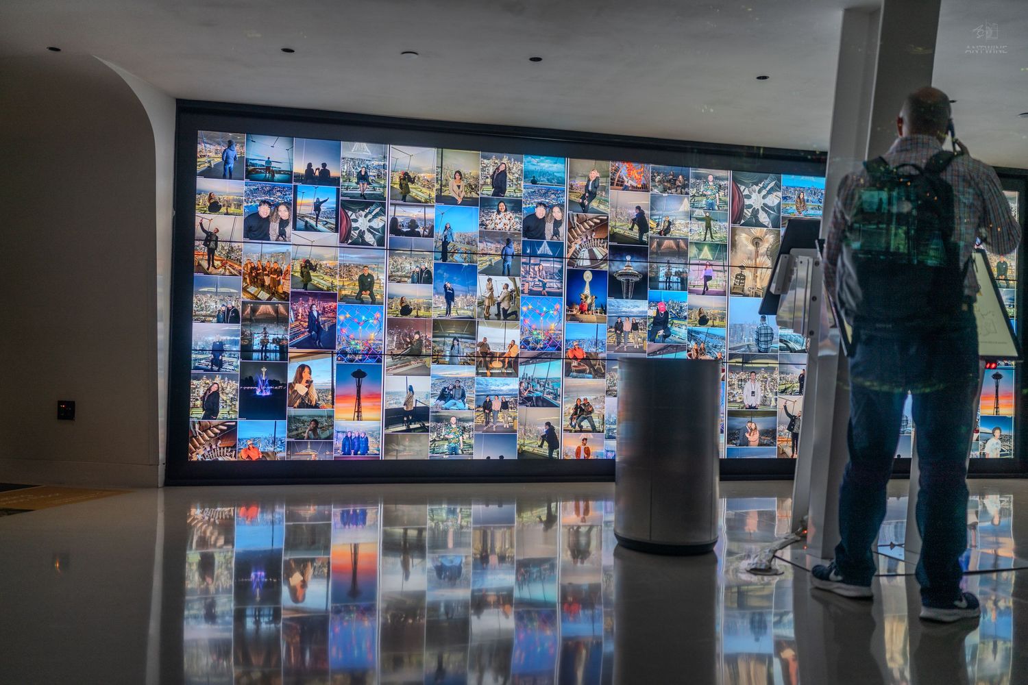 Person viewing large digital photo wall display in modern building lobby.