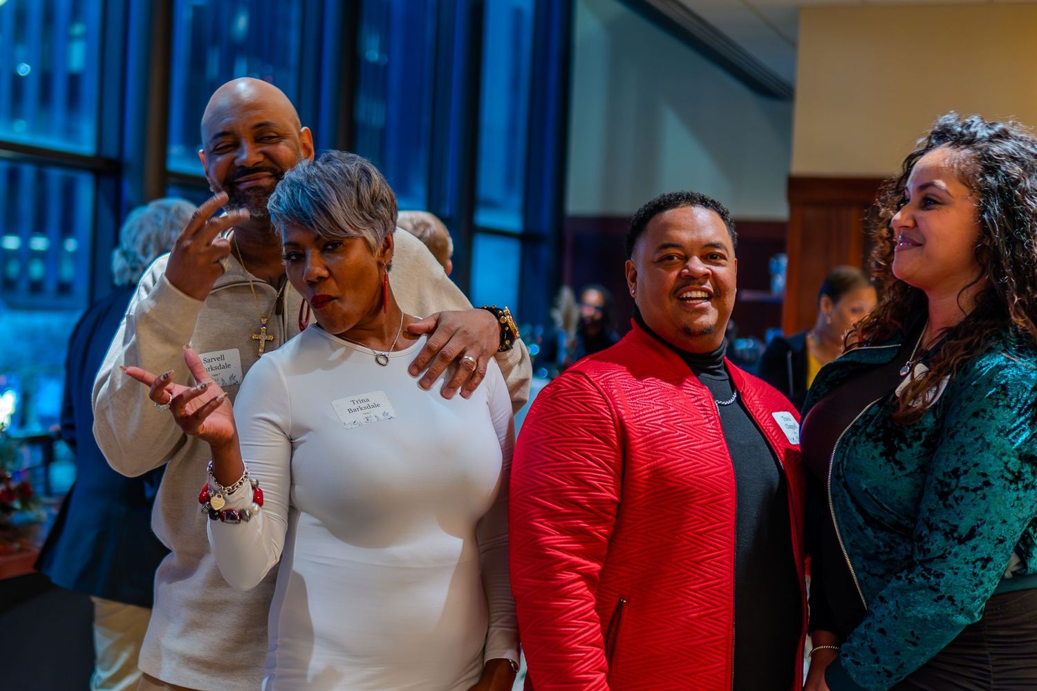 Group of four people smiling and posing together at a formal indoor event, dressed in elegant attire.
