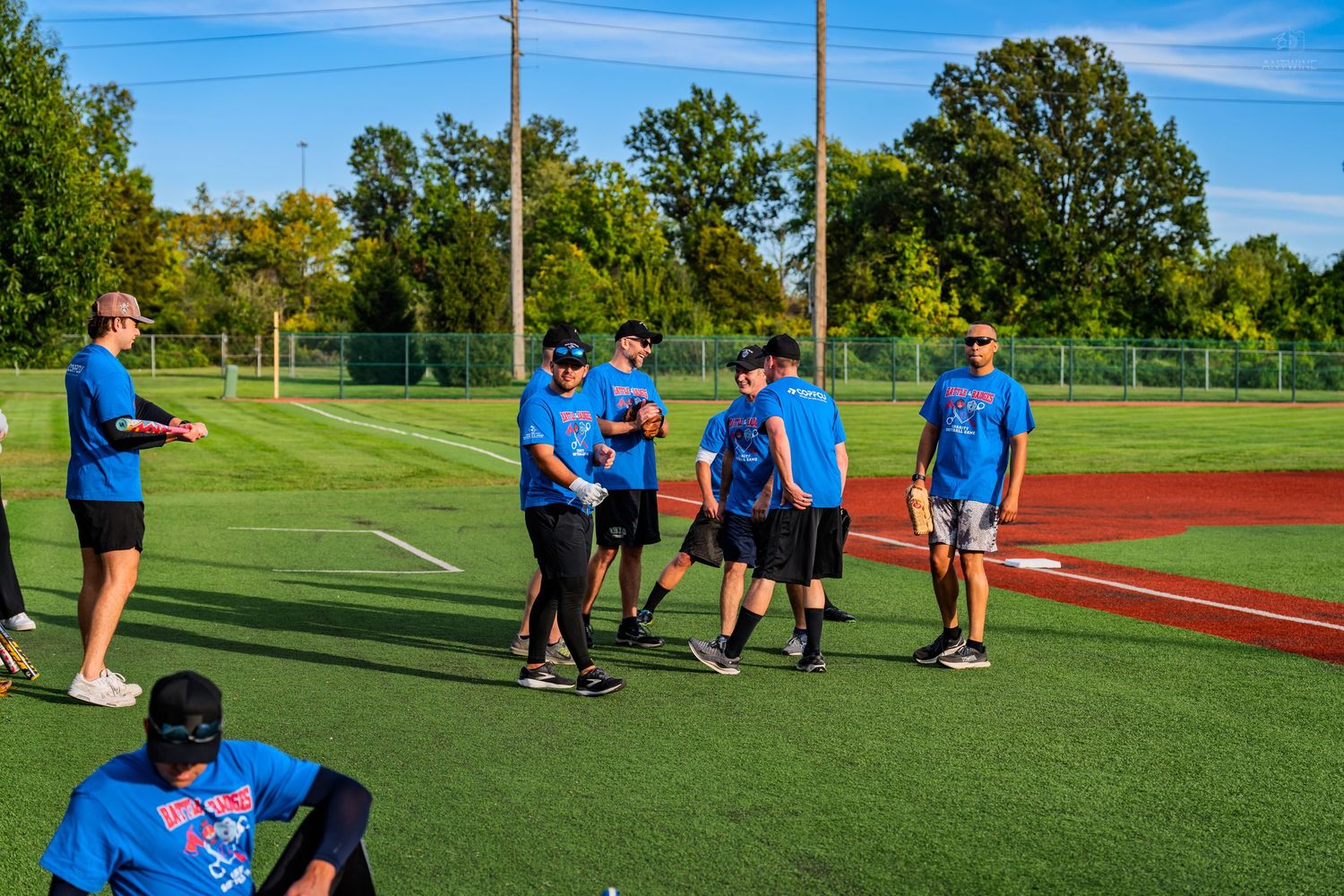 Group of people in blue shirts gathered on a baseball field during a sunny day outdoor sports event.