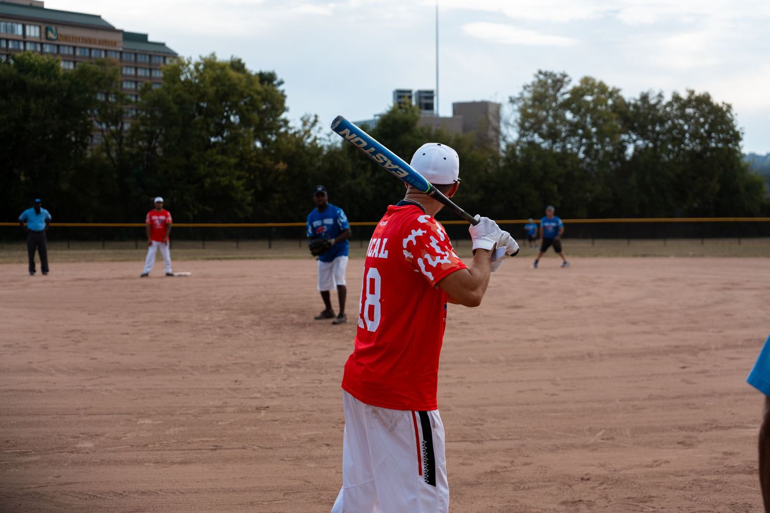 A batter in a red jersey number 18 prepares to swing during an outdoor softball game.