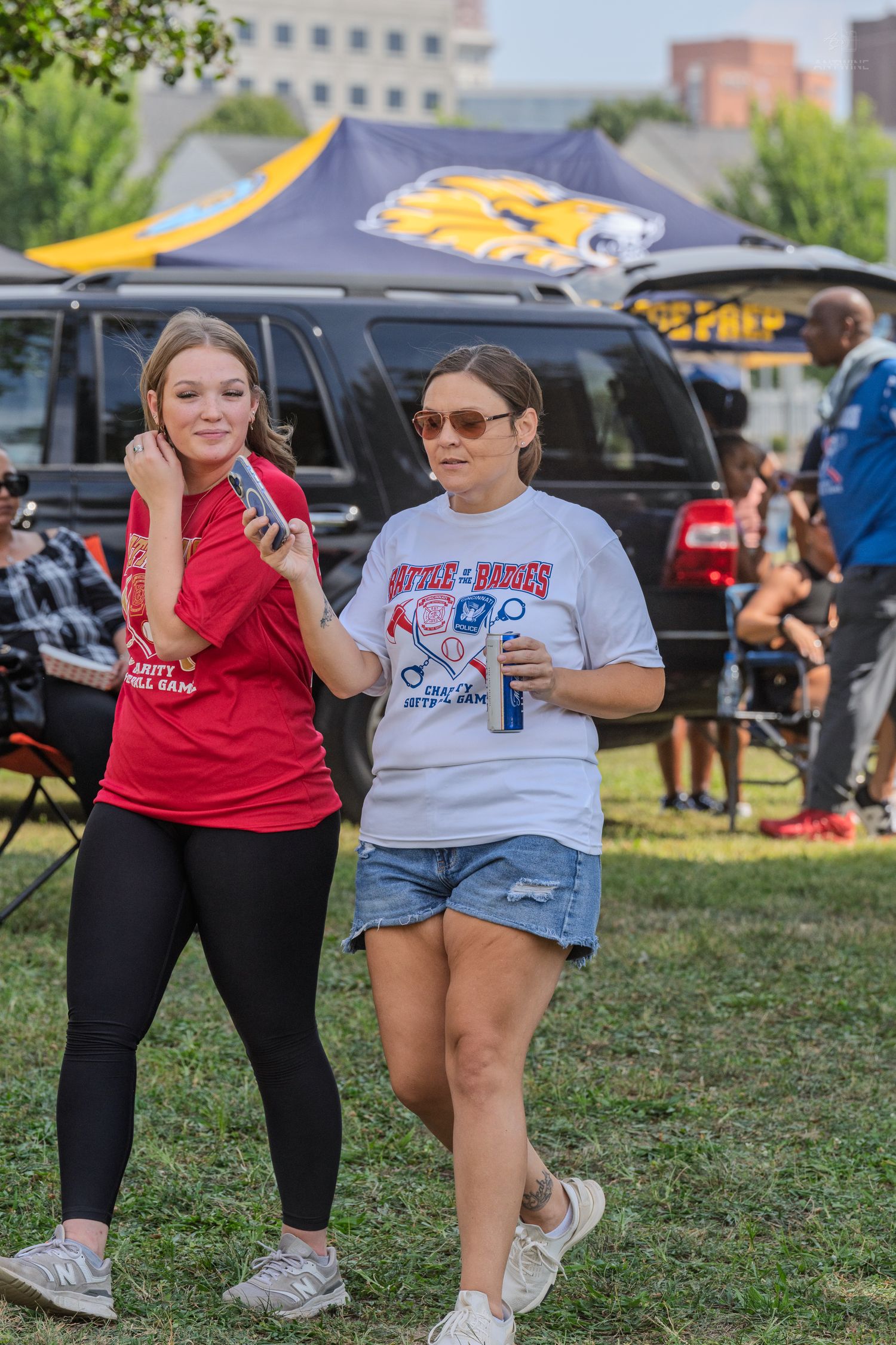 Two women walking together at an outdoor tailgate event near a yellow tiger mascot tent.