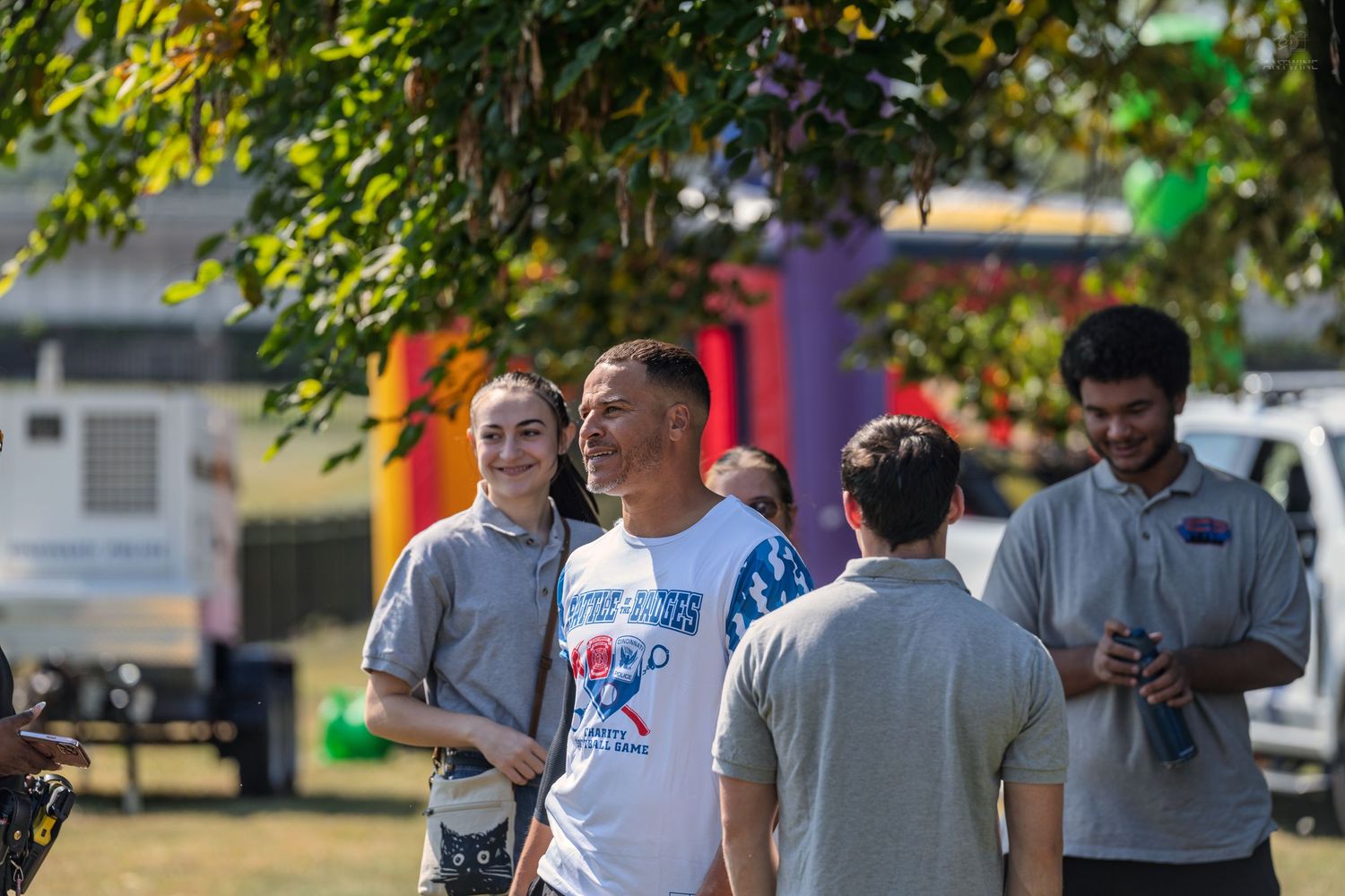 Group of people in gray shirts socializing outdoors at a sunny community event with colorful inflatables in background.