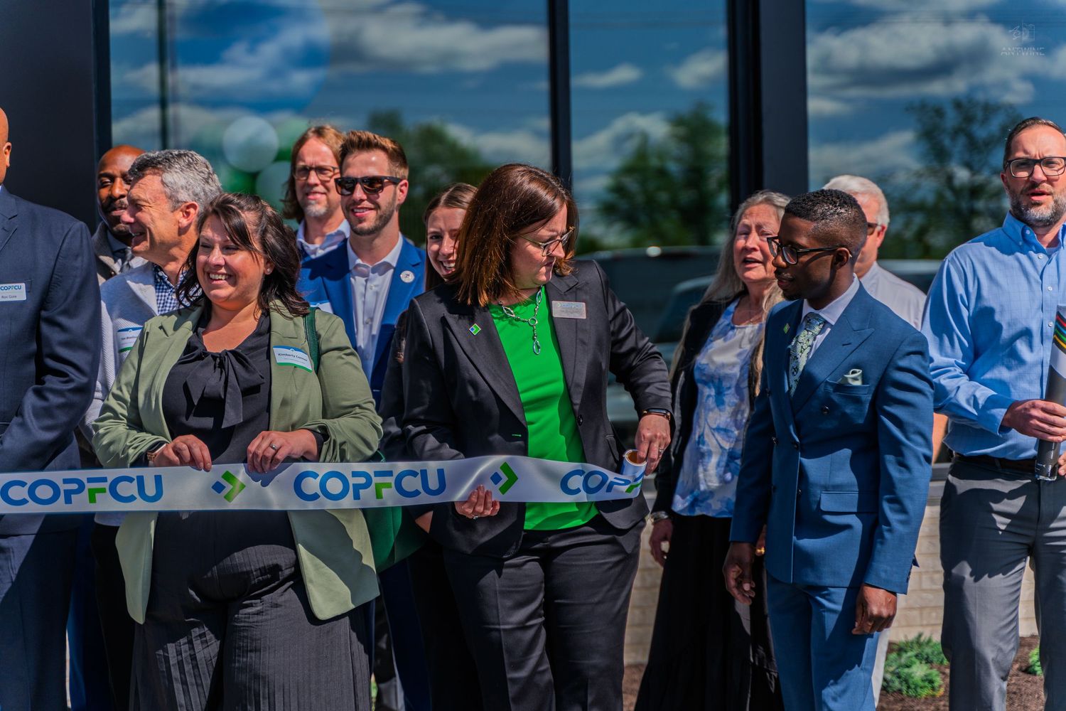 COPFCU credit union grand opening ribbon cutting event with diverse group of smiling employees and officials outside.