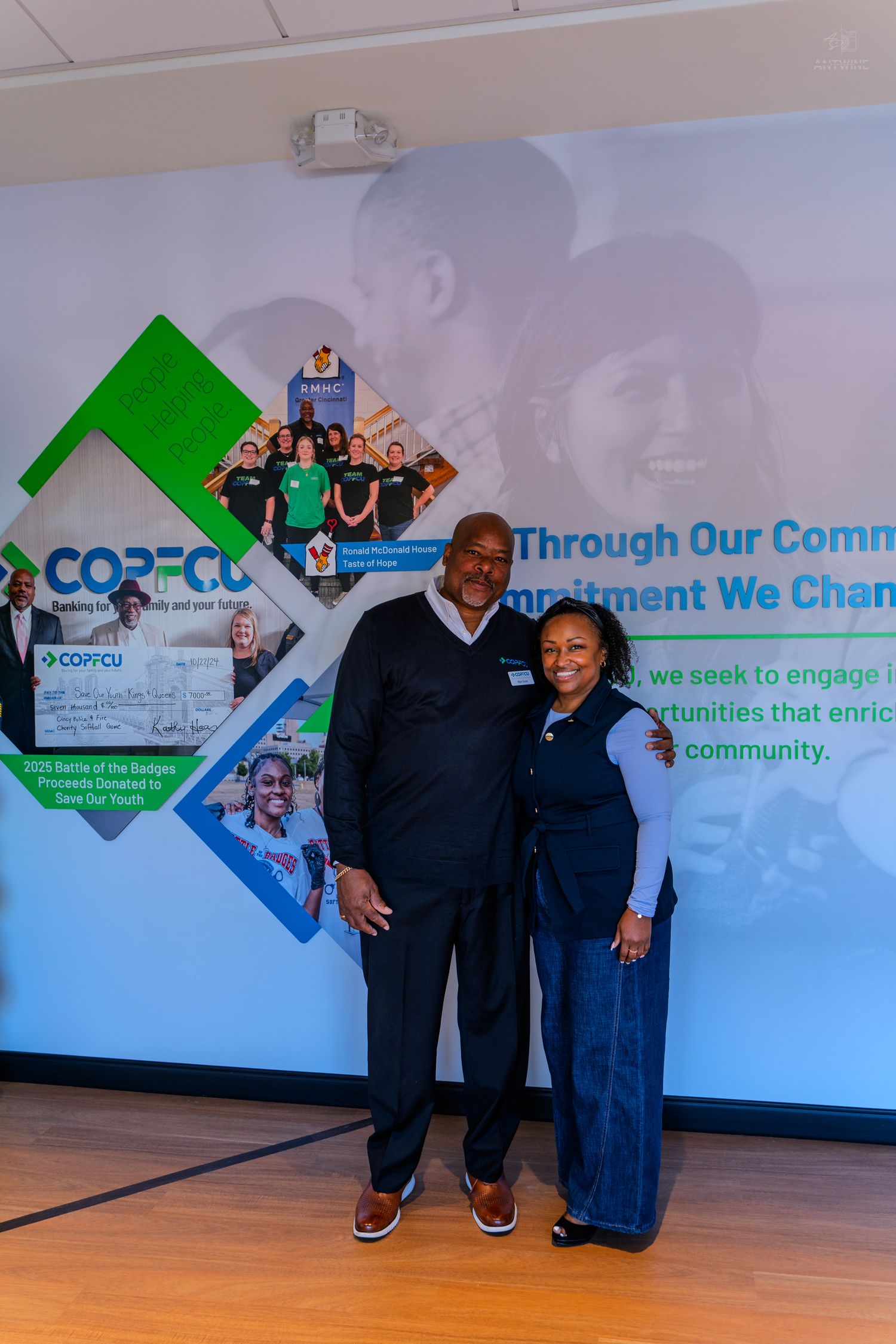 Two professionals pose together in front of a CORPCU community commitment banner at a credit union event.