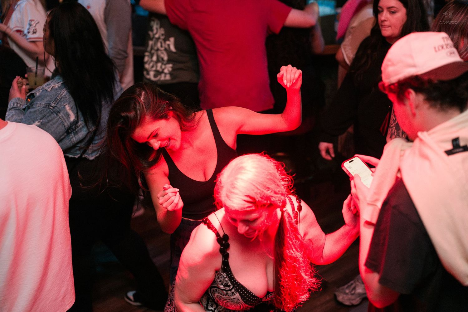Women dancing enthusiastically on a crowded dance floor under red lights at a nightclub.