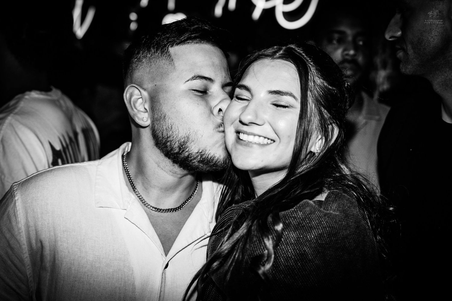 Black and white photo of a man kissing a smiling woman on the cheek at a nightclub.
