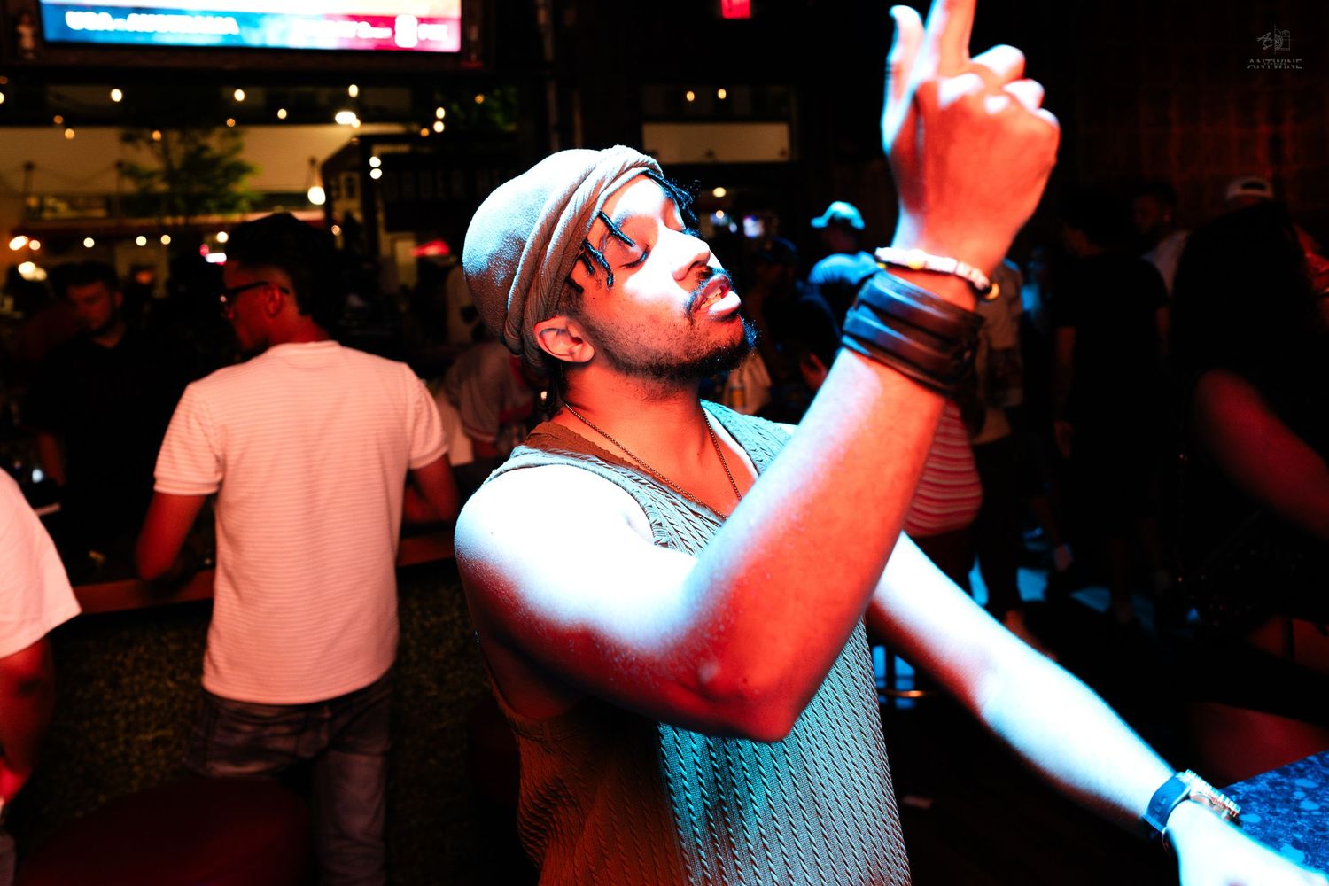 Man in cap dancing enthusiastically under blue lights at a lively outdoor nighttime party event.