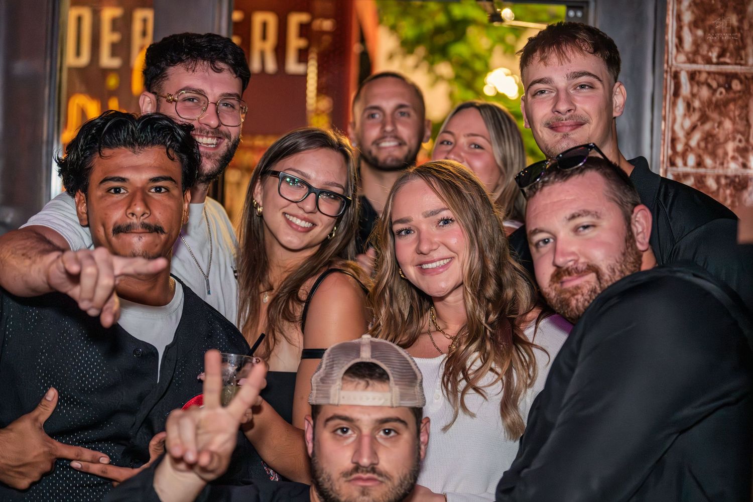 Group of smiling young adults taking a close-up group photo outside a nightclub.