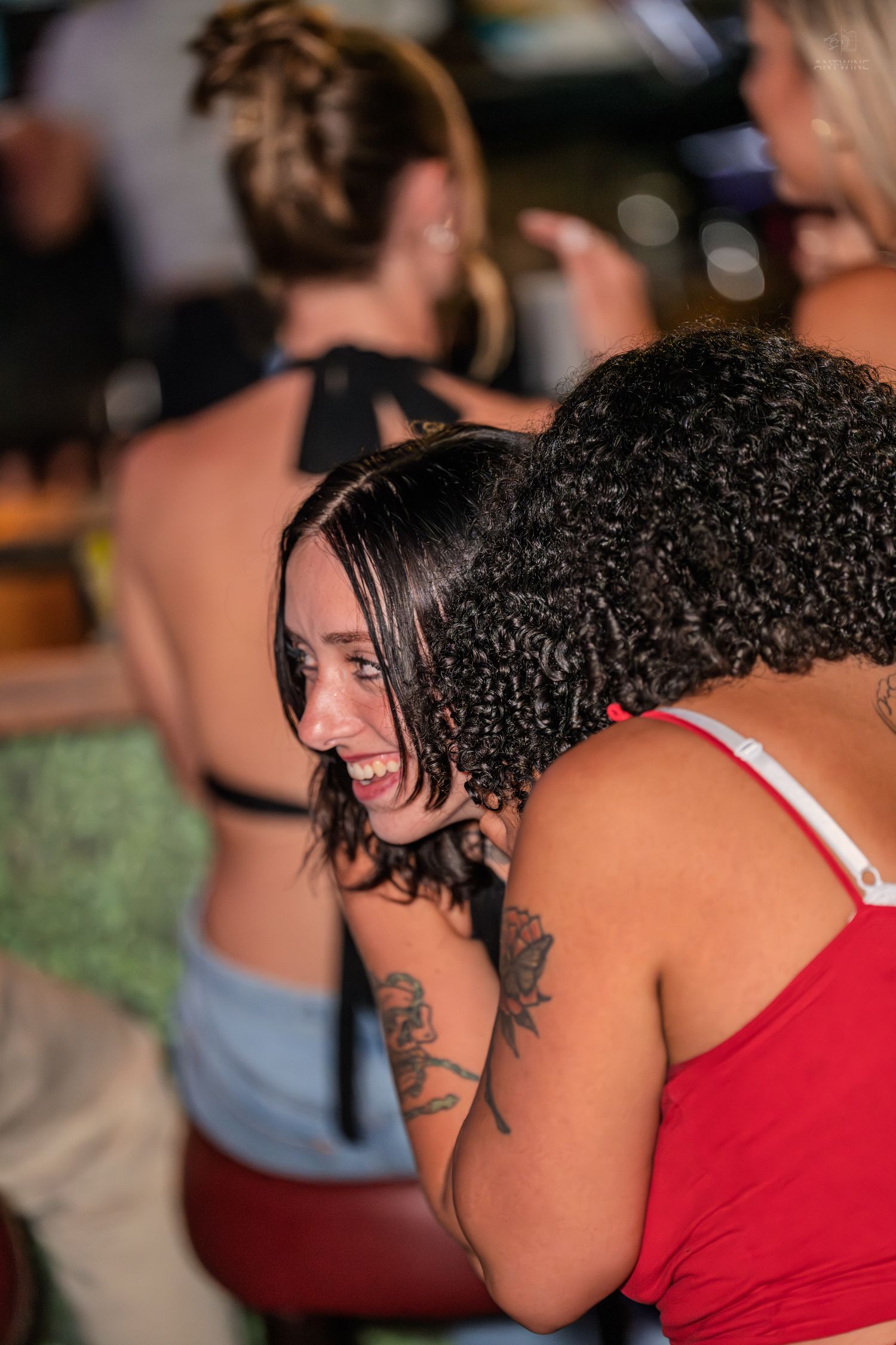 Two women laughing and embracing at a lively bar event.