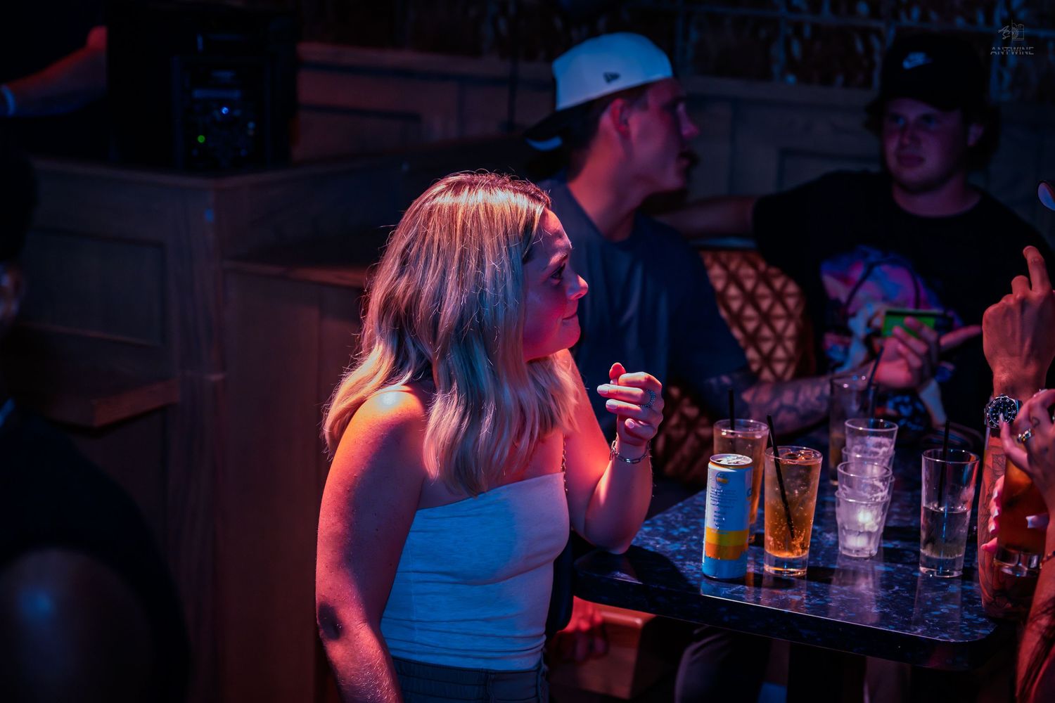 A blonde woman in a white top smokes near a bar table with drinks in a nightclub.