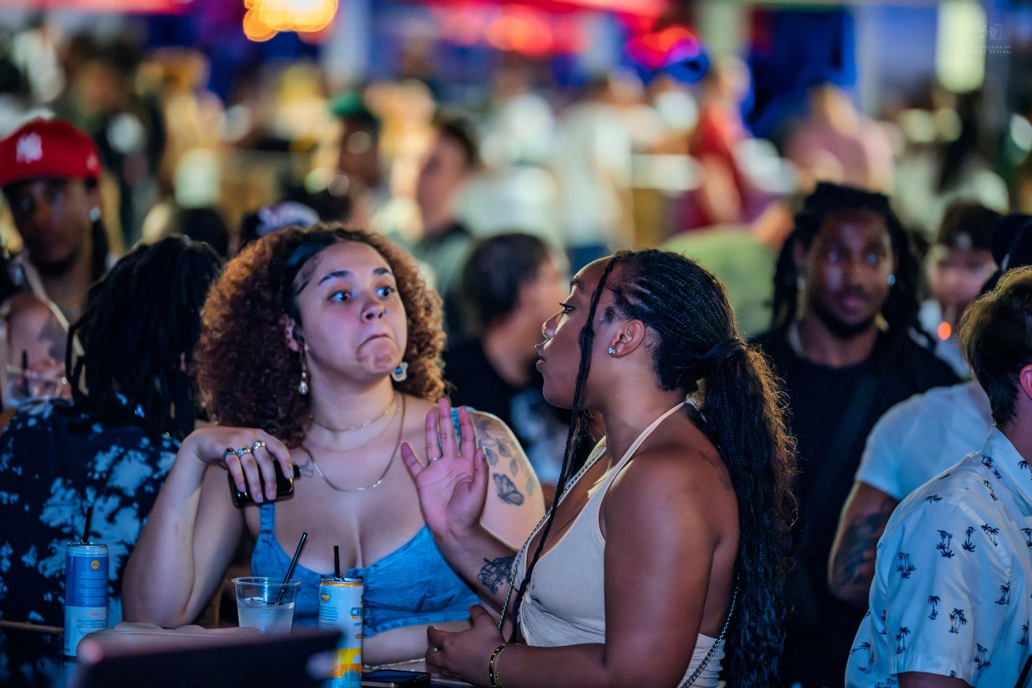 Two women having an animated conversation at a lively outdoor nightclub event.