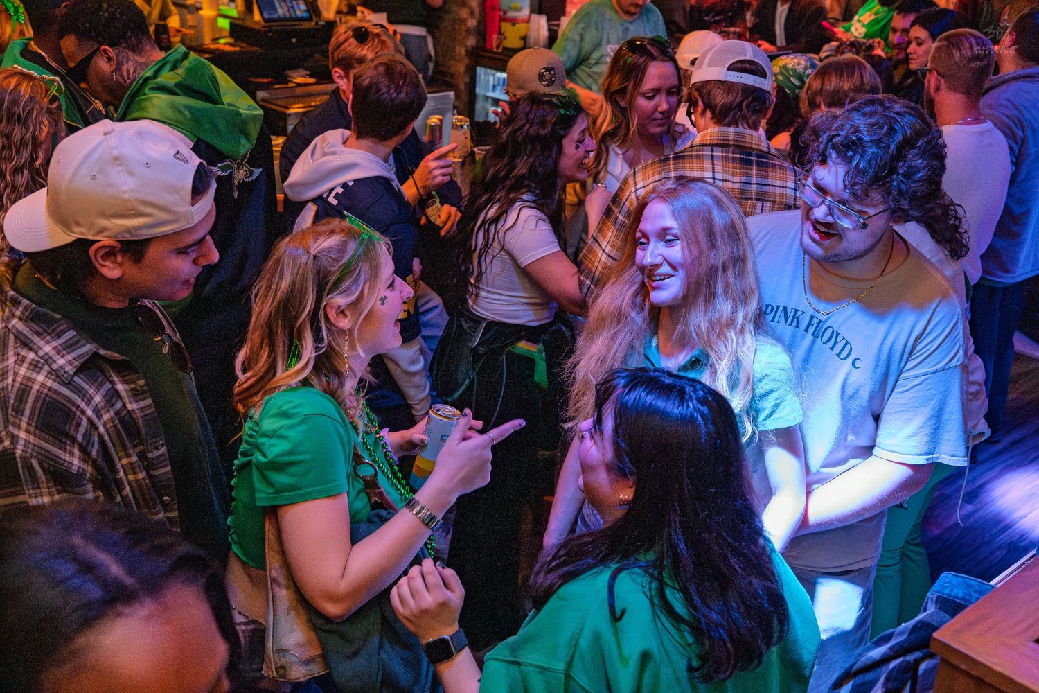 Crowd of young people in green outfits socializing at a lively St. Patrick's Day bar event.