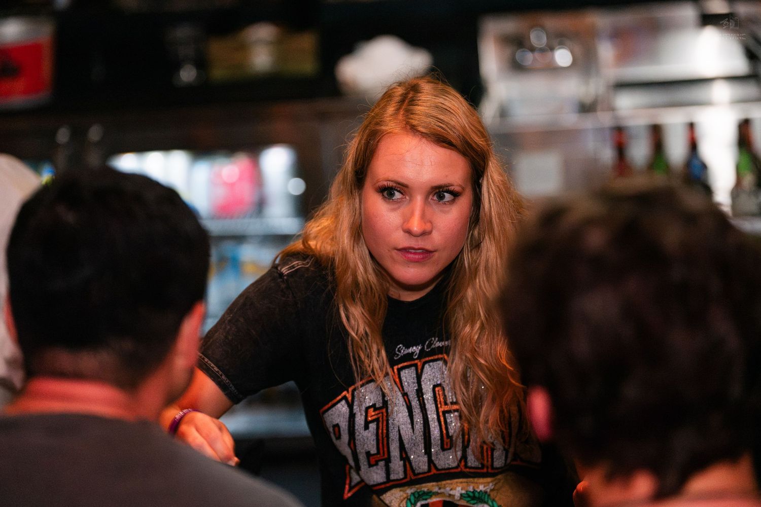 Blonde woman in Bengals shirt leaning forward at a busy sports bar event.
