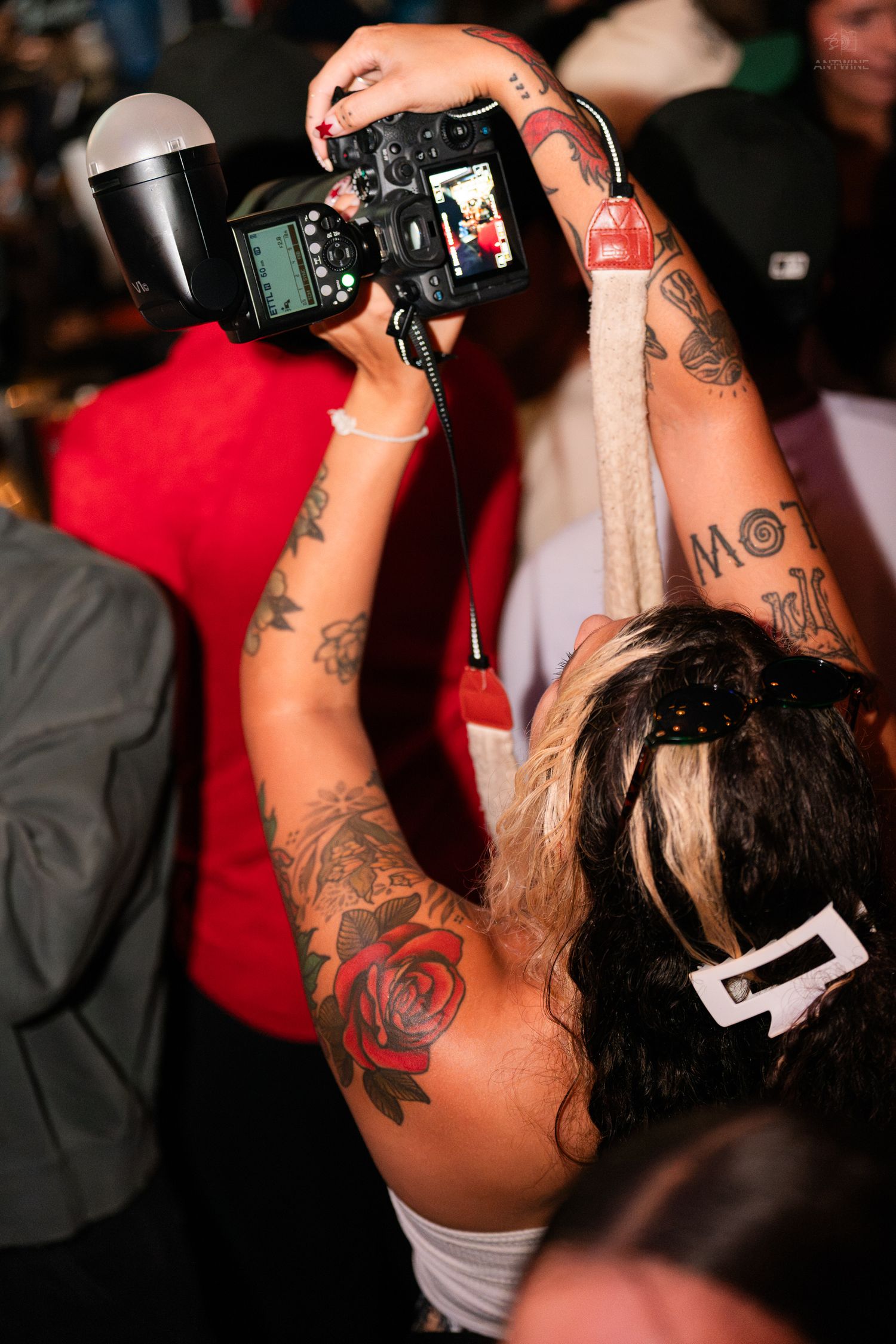 A heavily tattooed woman holds up a camera with flash to photograph at a party.
