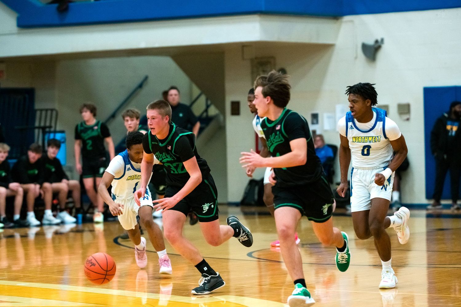 Green-uniformed players push fast break down court in high school basketball game.
