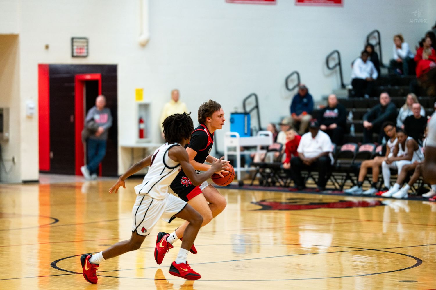 Two high school basketball players battle for possession as one drives past a defender on the court.
