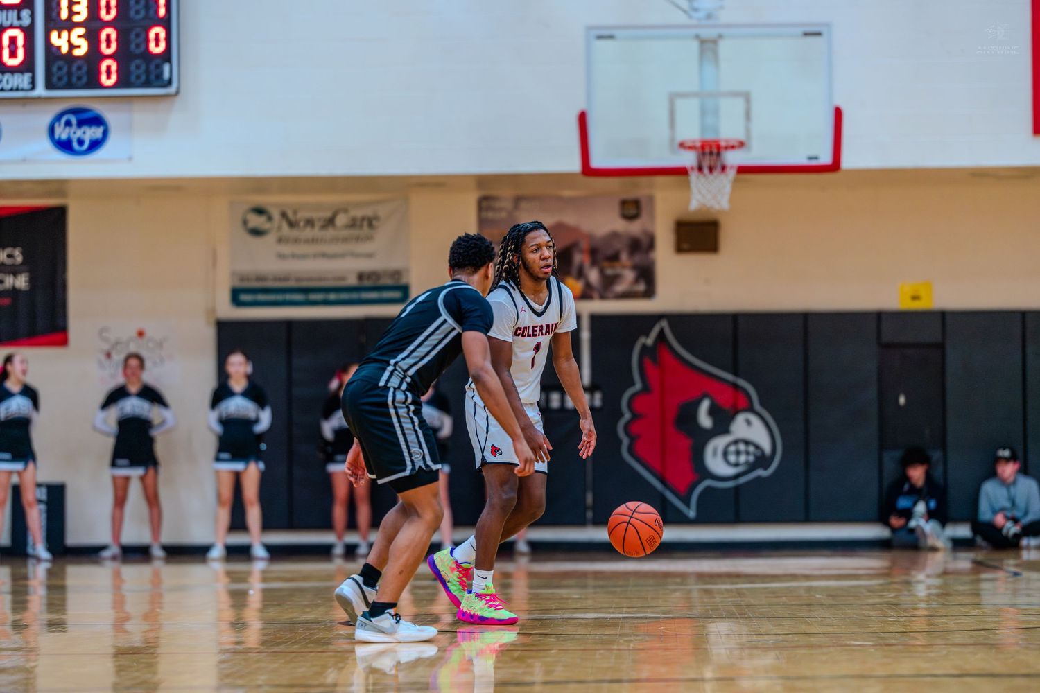 Colerain Cardinals basketball player dribbles against defender during high school game in red and white gymnasium.