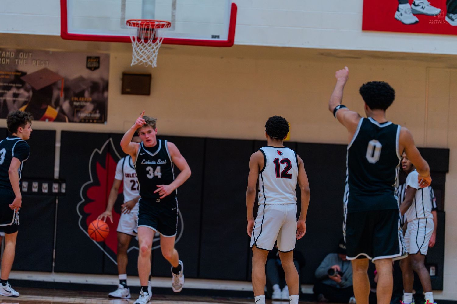 High school basketball player #34 dribbles upcourt as teammates #12 and #0 set up the offense.