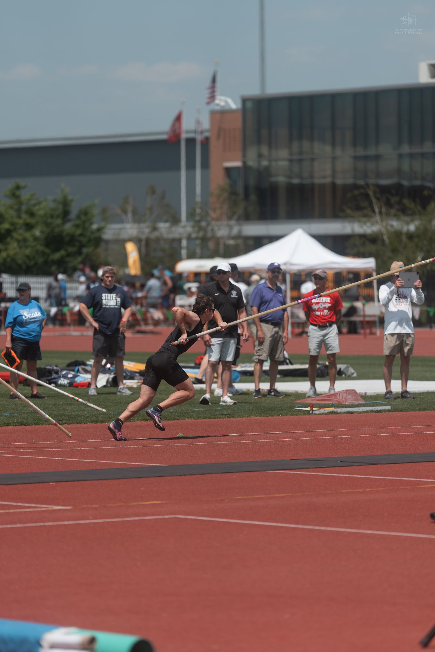 Athlete sprints down the runway carrying a pole vault pole at an outdoor track and field competition.