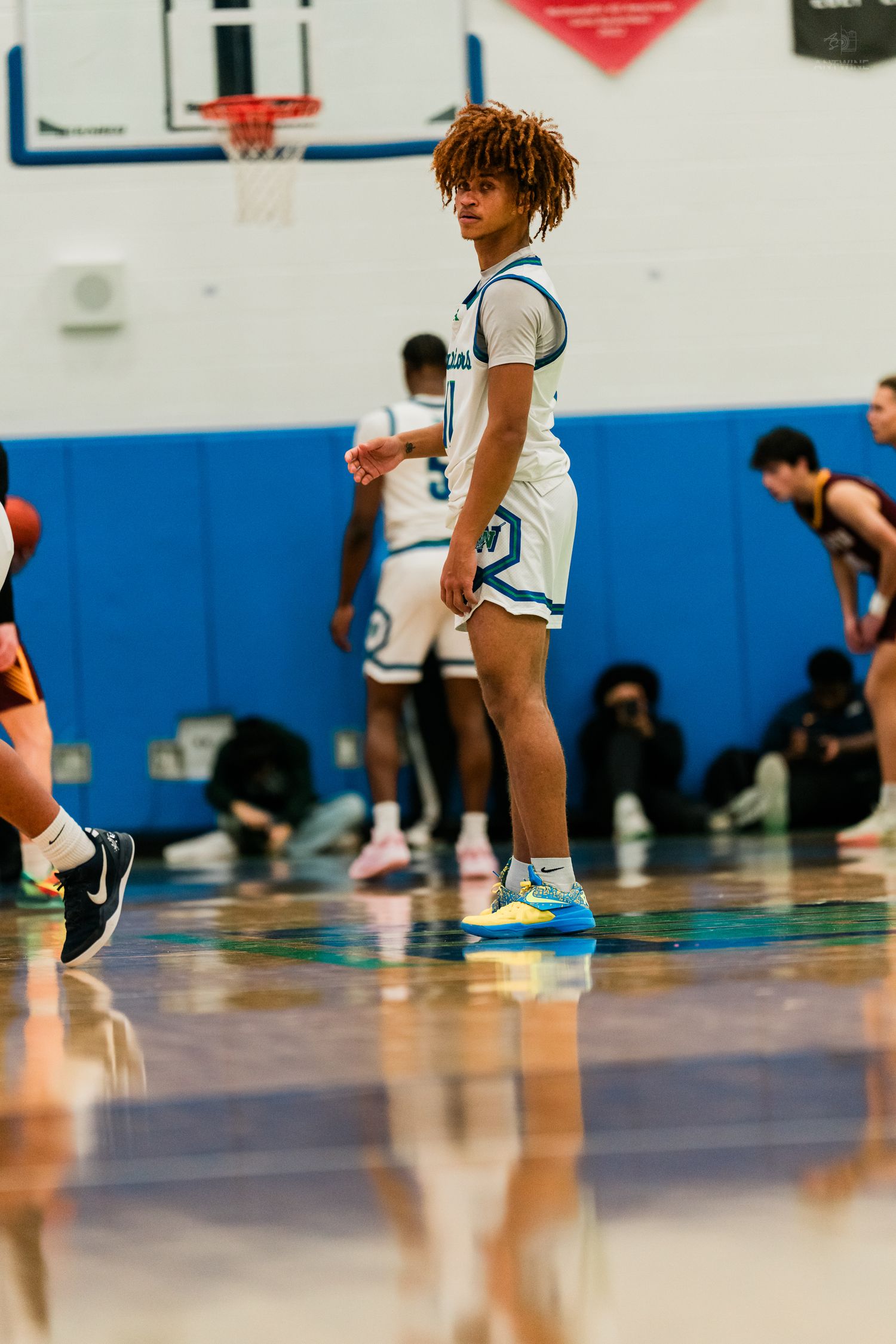 Warriors basketball player with curly hair stands on court during a high school game.