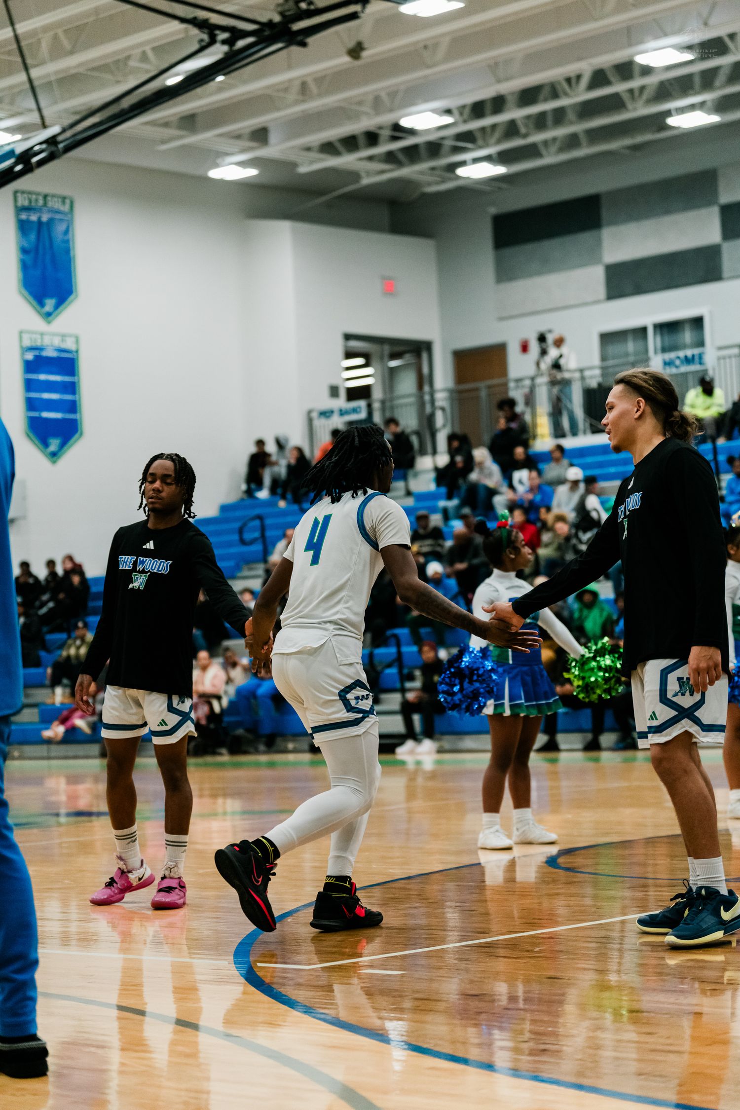 Basketball player #4 runs onto court during pregame introductions at Winton high school gym with cheerleaders.