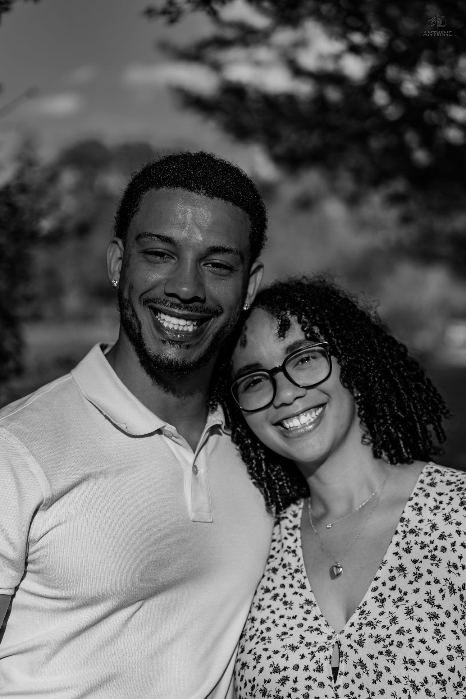 Smiling Black couple posing cheek to cheek in a park for a black and white engagement photo.
