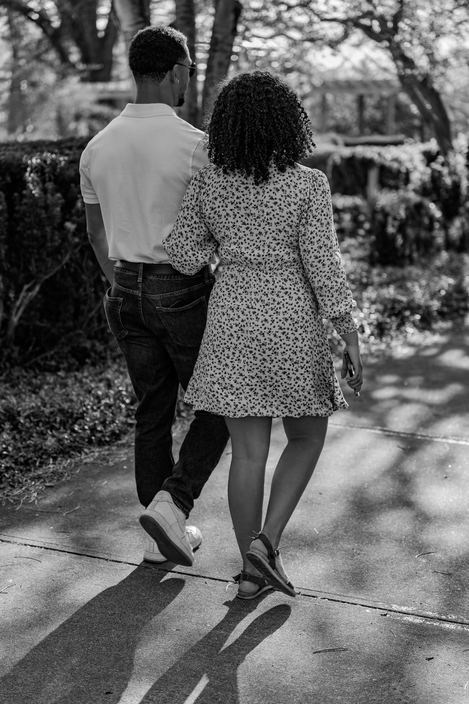 A couple walking side by side on a shaded park path in a classic black and white photograph.