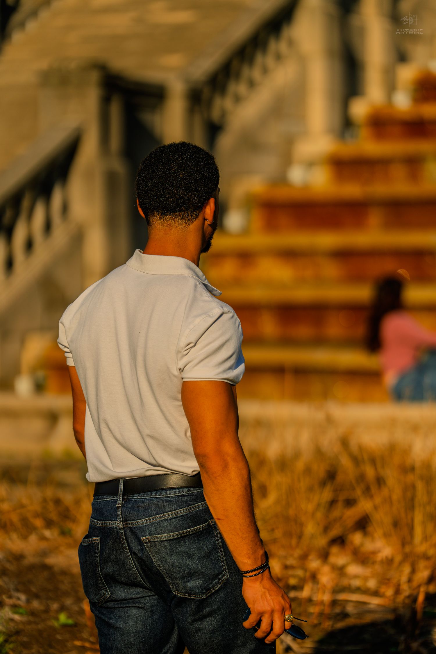 Man in a white t-shirt and jeans standing with his back turned near stone steps.