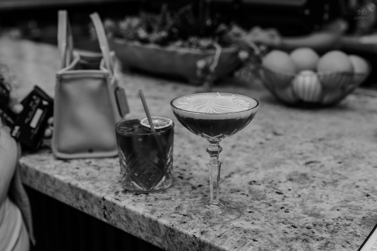 Two cocktails on marble surface with handbag and fruit bowl in black and white.