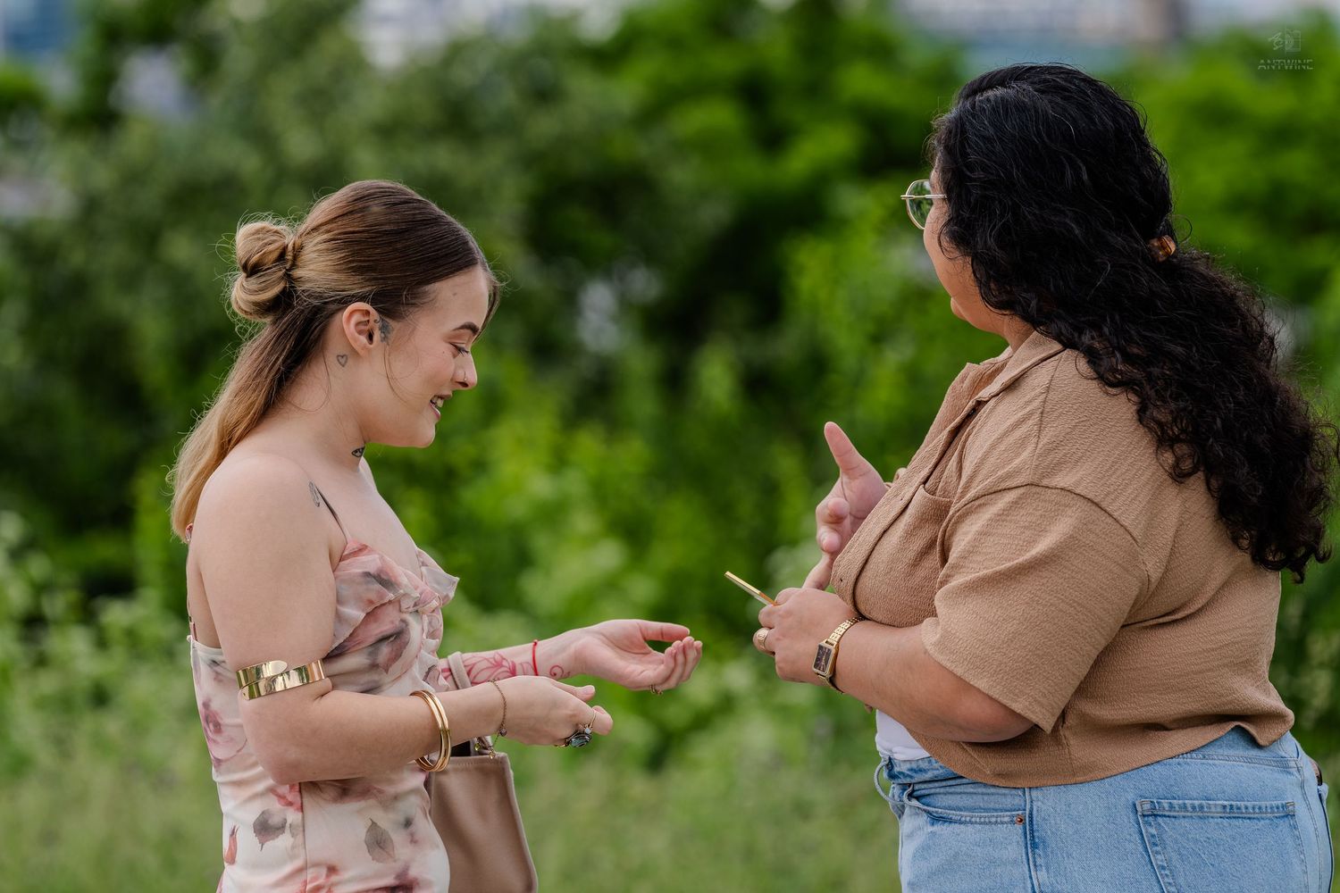 Two women examining an engagement ring together outdoors surrounded by vibrant green foliage.